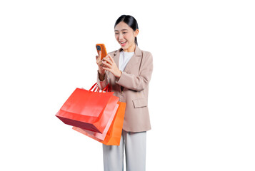 A surprised and excited young Asian woman holding shopping bags looks away from her smartphone with...
