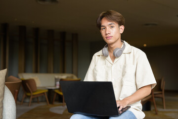 Non binary Asian student man sitting in modern coffee shop using laptop computer
