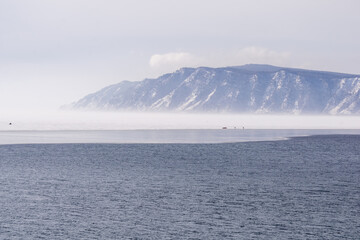 Serene landscape featuring calm waters reflecting distant mountains shrouded in mist, creating a...