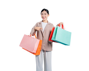 A cheerful young Asian woman holds several shopping bags and points with her index finger towards...