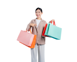 A cheerful young Asian woman holds several shopping bags and points with her index finger towards them, as if recommending a product or highlighting a great deal, isolated on a solid png background.

