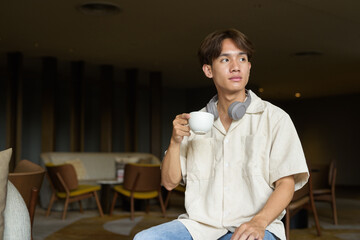 Non binary Asian student man sitting in modern cafe drinking coffee