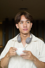 Non binary Asian student man sitting in modern cafe drinking coffee