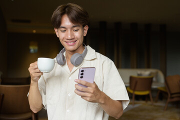 Non binary Asian student man sitting in cafe drinking coffee and using phone