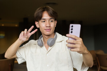 Non binary Asian student man sitting in modern coffee shop using phone