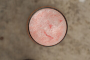 A glass of pink liquid with bubbles in itu. The bubbles are small and scattered throughout the liquid 