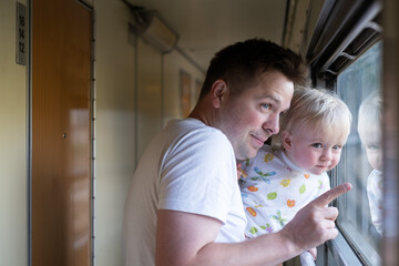 father, traveling with his little toddler by train, looking at the window. 