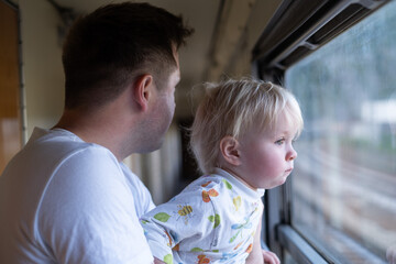 father, traveling with his little toddler by train, looking at the window. 