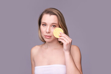 Young caucasian female applying facial sponge for skincare against purple background.
