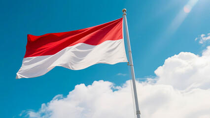 The Indonesian red and white flag flies proudly on a tall pole against a bright blue sky. Taken from a low angle, this realistic photo conveys the spirit of nationalism and national pride.