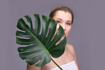 Caucasian female adult with monstera leaf, natural beauty and skincare concept on grey background.