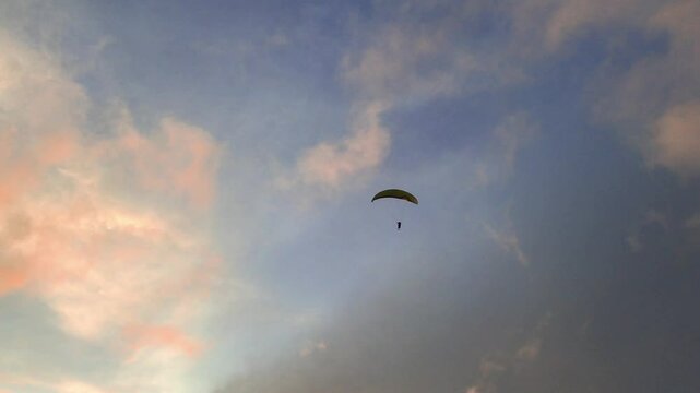 Paraglider flying against colorful sunset sky and clouds