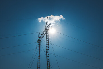 Electricity pole power transmission line against blue sky with shining sun
