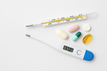 Digital clinical thermometer displaying mercury fever measurement with various pills and medication, blank space on the left side