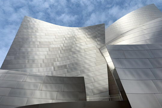 Los Angeles, California, USA - April 18, 2024: Curved stainless steel facade of Walt Disney Concert Hall against blue sky with clouds