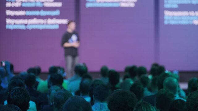 Blurred image of a presenter on stage during a professional conference with an audience in a corporate setting focusing on technology and innovation