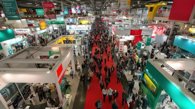 A bustling trade show floor is captured from an elevated perspective, showcasing a dynamic scene of industry networking and commercial exhibitions.