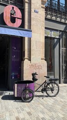 Barcelona, Spain - March 31, 2025: Black cargo bicycle parked outside a shop with purple cart and...