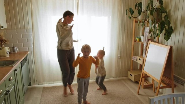 Family Moments Dancing Together in a Cozy Kitchen Filled with Joy and Love, enjoying time with her children. A joyful scene of a mother dancing with her little kids. Mom dance with son and daughter.