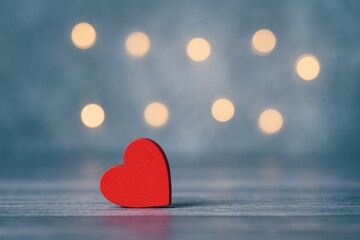 Fototapeta premium Stock image of a tiny crimson wooden heart against a bluish backdrop with blurred light bulbs