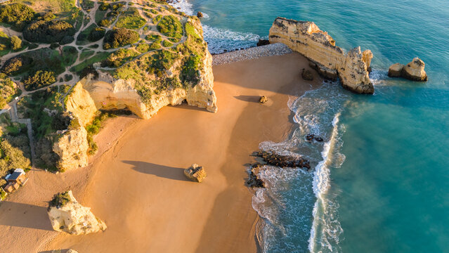 Aerial view of golden sands meet the turquoise waters, cliffs rise majestically, creating a stunning contrast of colors at Praia do Camilo, Lagos, Algarve, Portugal.