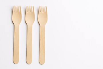 Eco-friendly disposable wooden cutlery arranged on a white background with three forks on the left side, highlighting sustainable materials and a flat lay design.