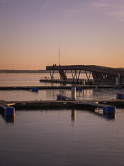 Obraz premium A peaceful sunset over the harbor in Senftenberg, Germany. The golden light reflects on the calm water and empty piers, creating a serene and tranquil evening atmosphere. Wind turbines are visible