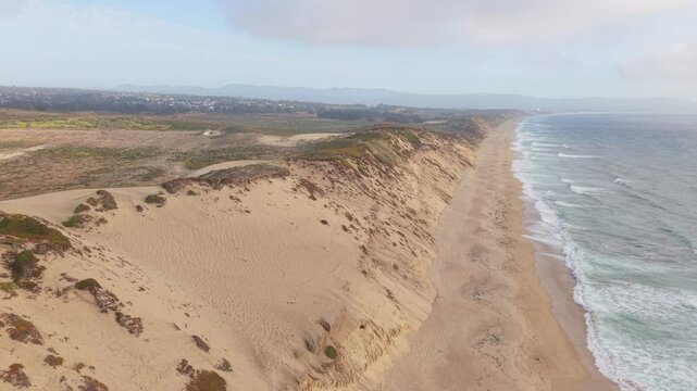 Static aerial shot in downward view over dunes, beach, and ocean at Fort Ord Dunes State Park, followed by a gentle elevation.