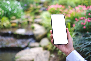 Mockup image of a woman holding mobile phone with blank white desktop screen in the nature outdoors