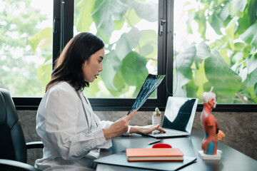 Female doctor examines an X-ray in a contemporary office setting, featuring a laptop and anatomical...