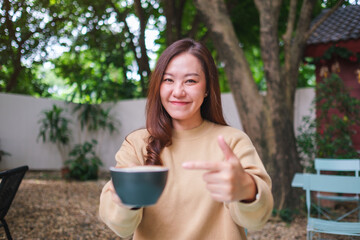Portrait image of a woman holding and pointing finger at a cup of coffee in the outdoors cafe