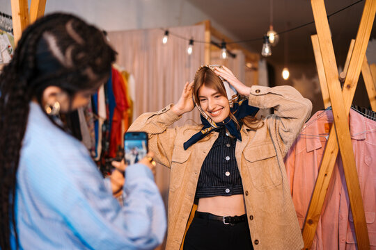 Fashionable Young Woman Posing in Clothing Shop with Friend Taking Photo