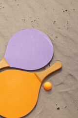 Beach tennis rackets and ball on sand. Active lifestyle, games and sports. Beach tennis set. Bright wooden rackets for outdoor games. Summer outdoor games. Summer sports and games concept. Close-up
