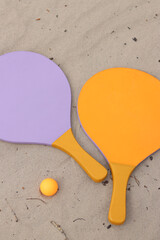 Beach tennis rackets and ball on sand. Active lifestyle, games and sports. Beach tennis set. Bright wooden rackets for outdoor games. Summer outdoor games. Summer sports and games concept. Close-up