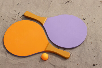 Beach tennis rackets and ball on sand. Active lifestyle, games and sports. Beach tennis set. Bright wooden rackets for outdoor games. Summer outdoor games. Summer sports and games concept. Close-up