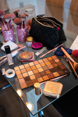 A living room table filled with makeup, including various cosmetics, brushes, palettes, and...