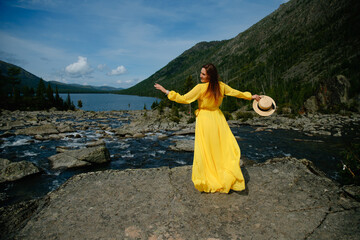 Young caucasian female in yellow dress by mountain lake with straw hat