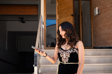 Arab young woman wearing an elegant black dress with intricate patterns looks at her phone while...