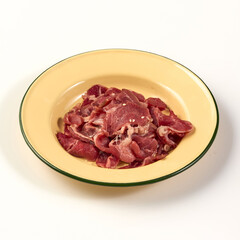 Thinly sliced raw beef arranged in yellow enamel plate with green rim, ready for cooking or grilling, showcasing its fresh and tender texture