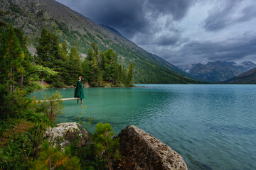 Love of Nature and people, Woman in green dress by mountain lake under dramatic sky