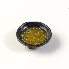 Small black bowl filled with green seafood dipping sauce, featuring mix of chili, garlic, lime, and herbs, placed on white background. sauce appears fresh and flavorful
