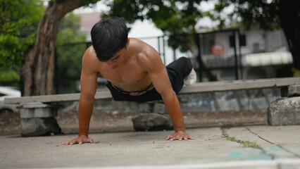 Asian man doing push-ups during street workout at public park.