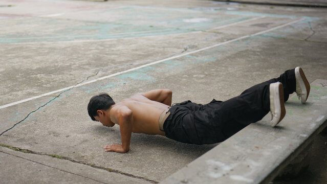 Asian man doing push-ups during street workout at public park.