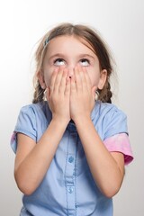 Young girl covering her mouth, looking up in surprise or shock.