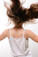 Girl with long brown hair spinning, viewed from behind. She wears a simple white tank top against a...