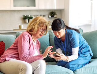 Doctor or nurse caregiver helping senior woman with a mobile phone at home or nursing home