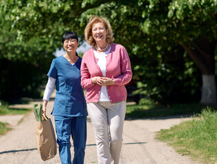 Nurse caregiver with senior woman walking outdoors and helping with shopping bag with groceries