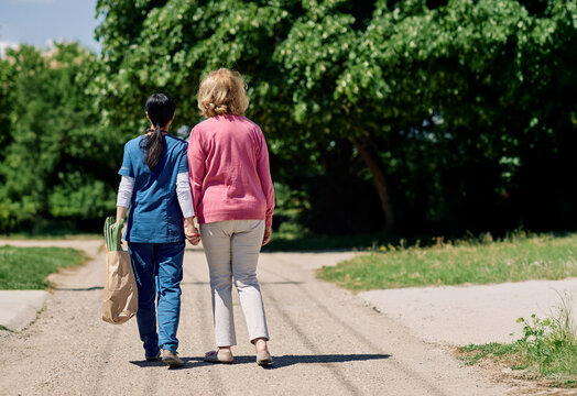 Nurse caregiver with senior woman walking outdoors and helping with shopping bag with groceries - Powered by Adobe