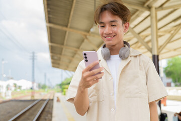 Young non binary tourist traveler in train station using phone