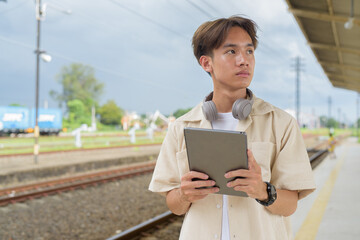 Young non binary tourist traveler in train station using digital tablet computer